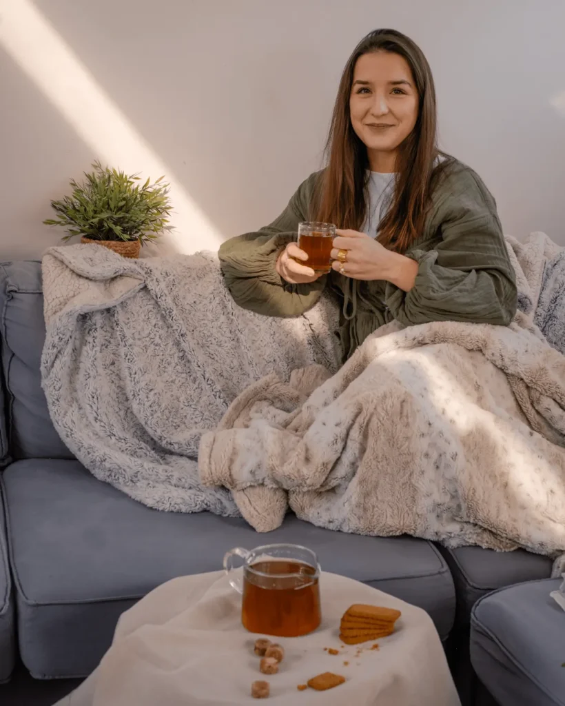 Femme buvant du thé Instan’T sur un canapé avec plaid et lumière naturelle.