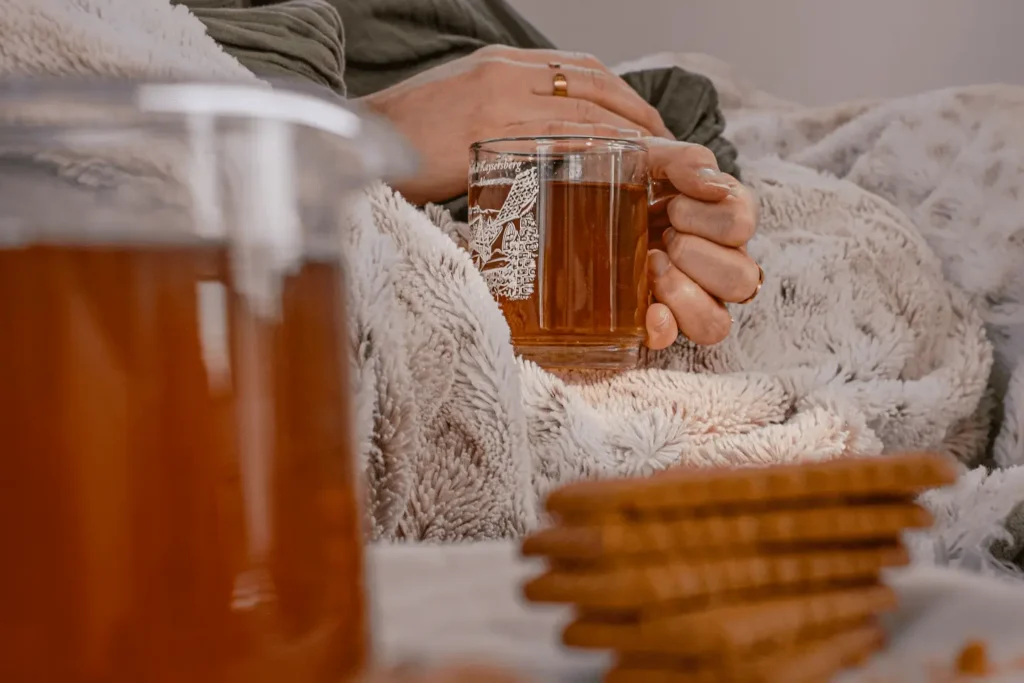 Mains tenant une tasse de thé sur un plaid dans une ambiance hivernale.