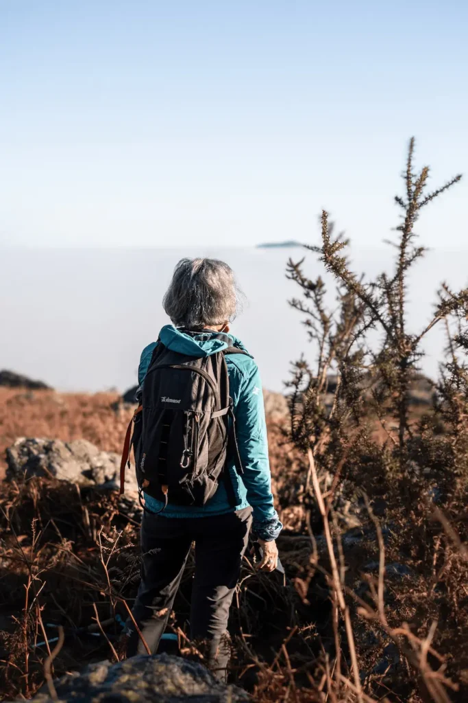 Une randonneuse contemple la mer de nuages depuis un sommet d’Ixassou. Le contraste entre ciel bleu et nuages blancs accentue la magie du moment.